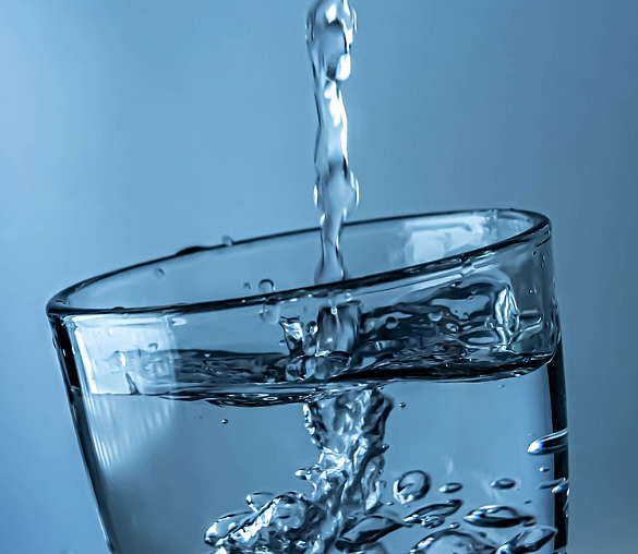 Fast volles Wasserglas, in das Wasser gekippt wird.  